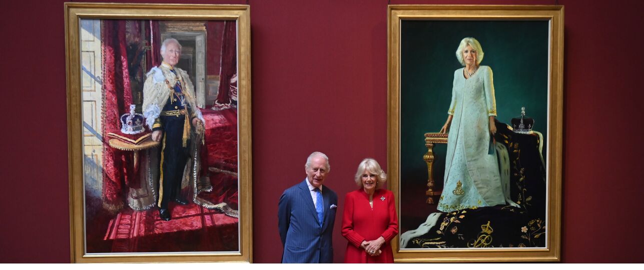 Koning Charles en koningin Camilla naast hun kroningsportretten.