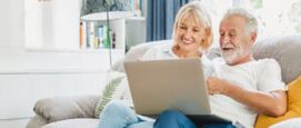Een seniore man en vrouw op de bank met een laptop op schoot die Startpagina als opstartpagina instellen en enthousiast zijn.